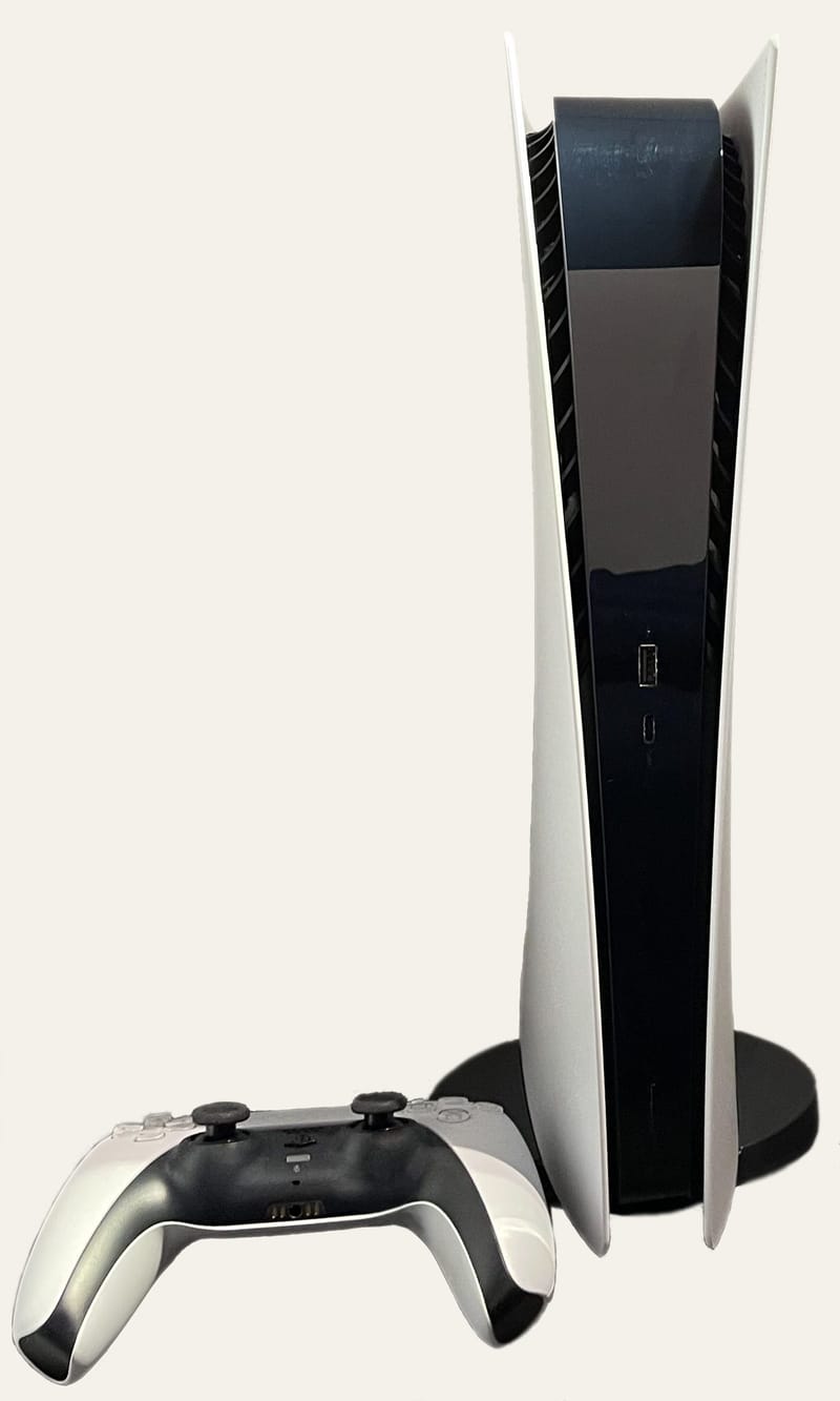 Una PlayStation 5 Digital Edition blanca estándar en posición vertical sobre su soporte, junto a un mando DualSense
