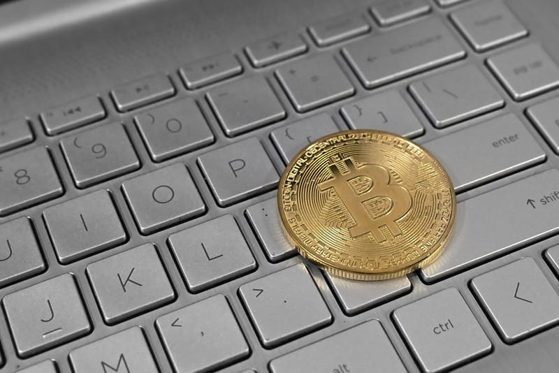A gold-coloured Bitcoin coin resting on the keys of a laptop keyboard
