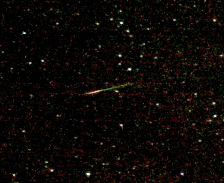 A green and red meteor streak crossing a dark, star-filled night sky